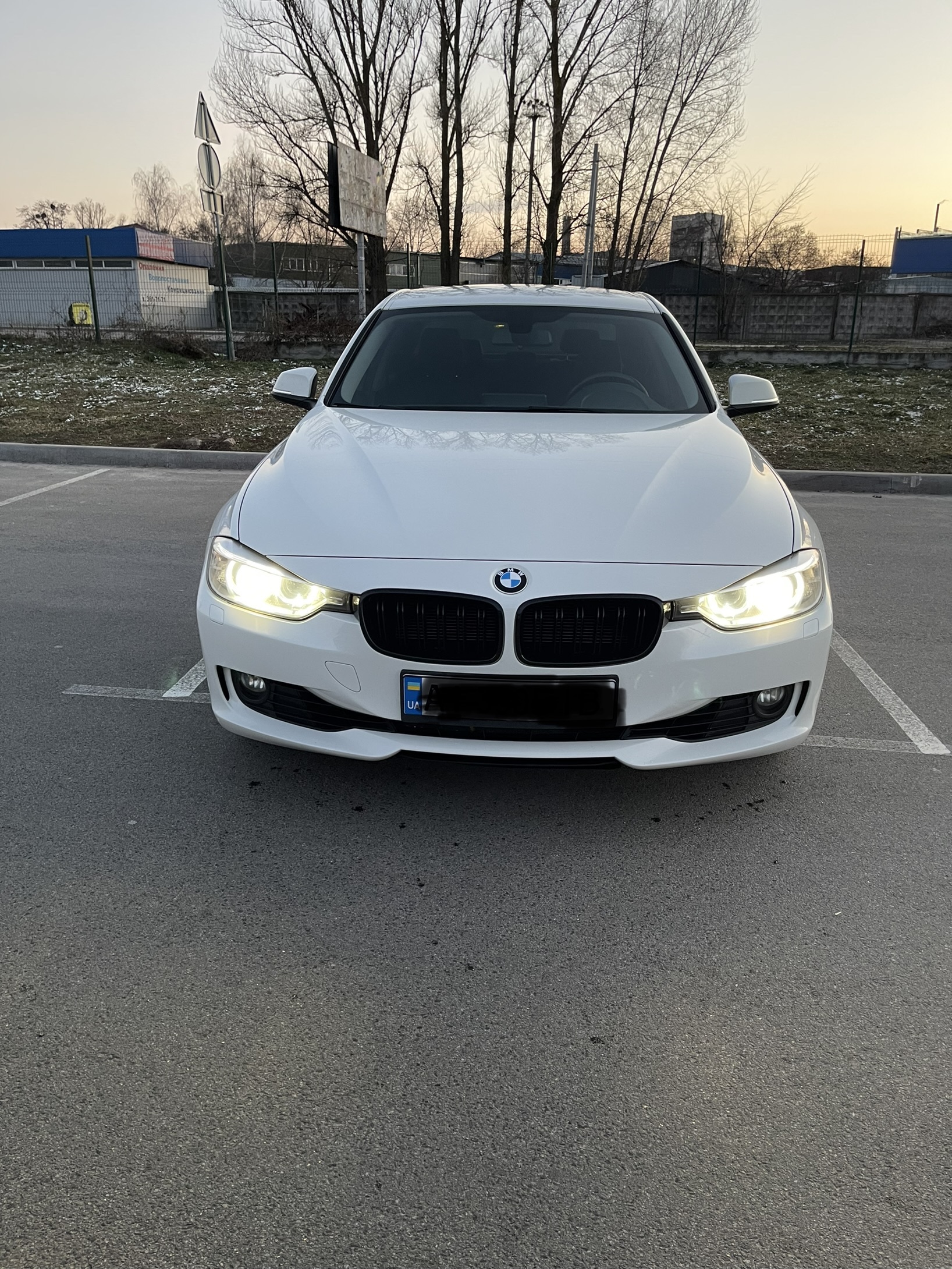 White BMW F30 320i front end at dusk with headlights on