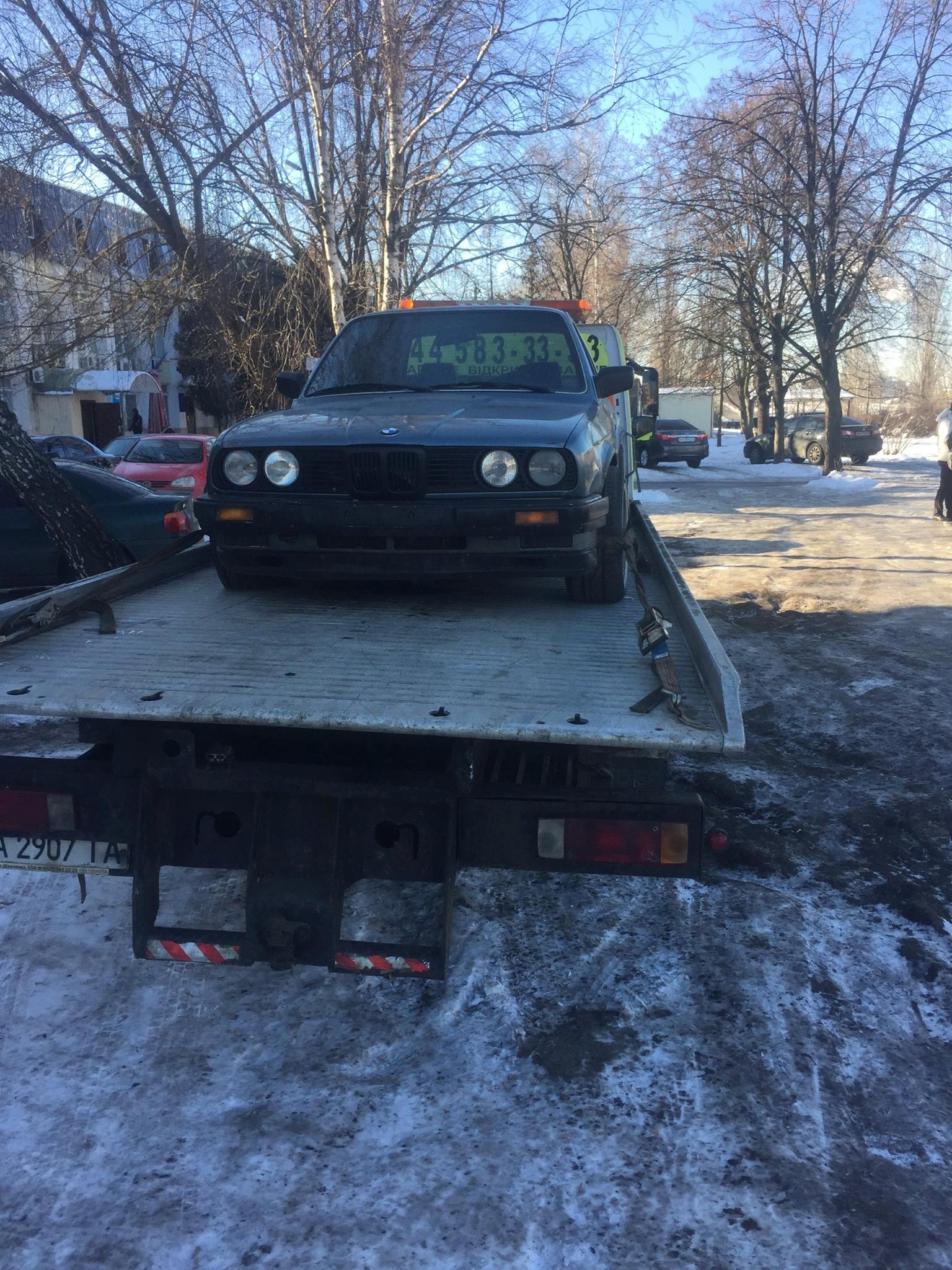 Grey BMW E30 arriving on a flatbed tow truck in winter