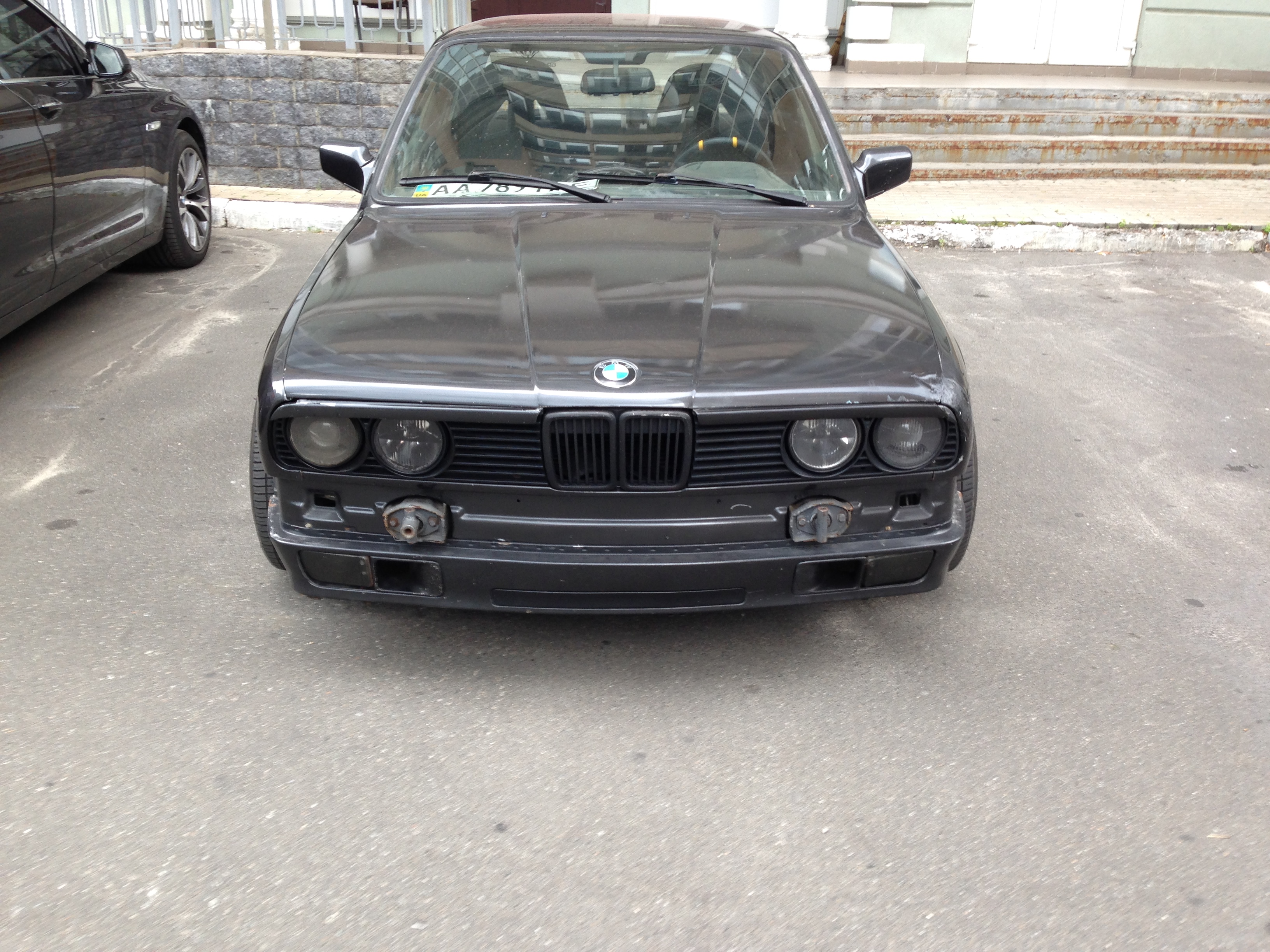 Black BMW E30 sedan front end with grille and quad headlights